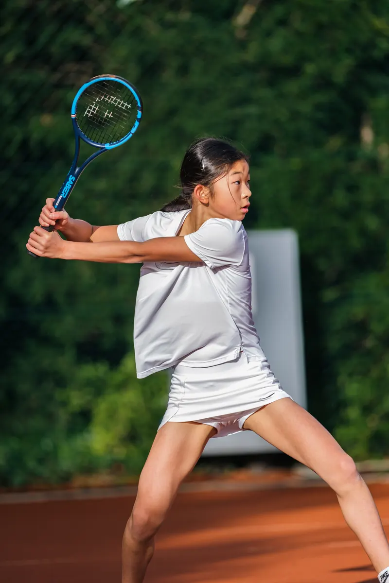 A junior player in a wide, balanced stance, set up early to hit a forehand with the Saber